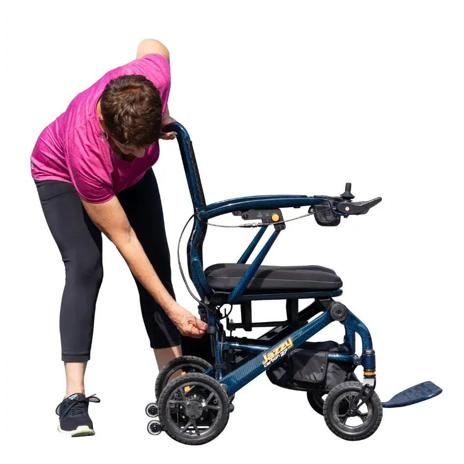 Jazzy Carbon 27 power wheelchair with woman in pink shirt folding the blue carbon fiber frame outdoors