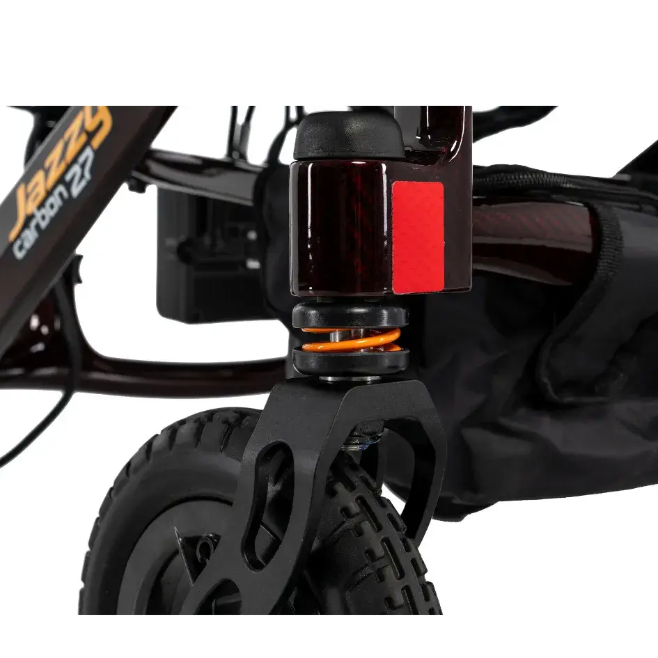 Power wheelchair front suspension close-up showing spring shock absorber, red reflector, and all-terrain front caster wheel
