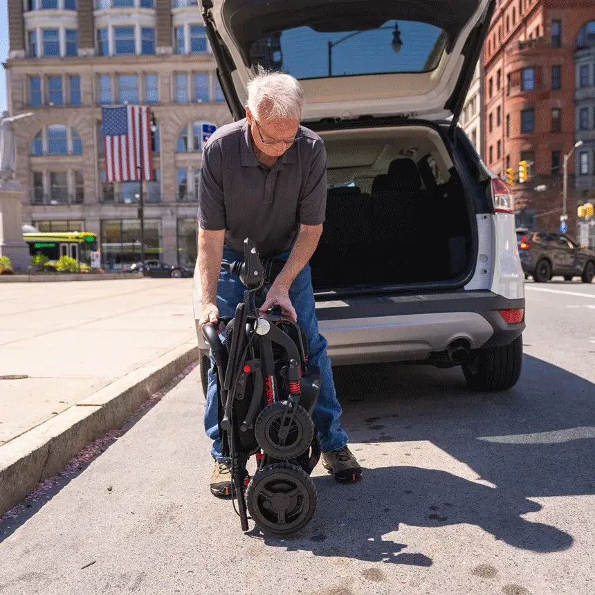 Folding power wheelchair being lifted from an SUV trunk by an older man on a city street