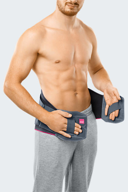 Lumbamed Facet lumbar support belt worn by a shirtless man, shown being fastened at the lower back with pink accents visible