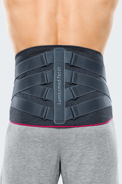 Lumbamed Facet lumbar support brace worn on a person's lower back, showing gray mesh fabric with structured straps and