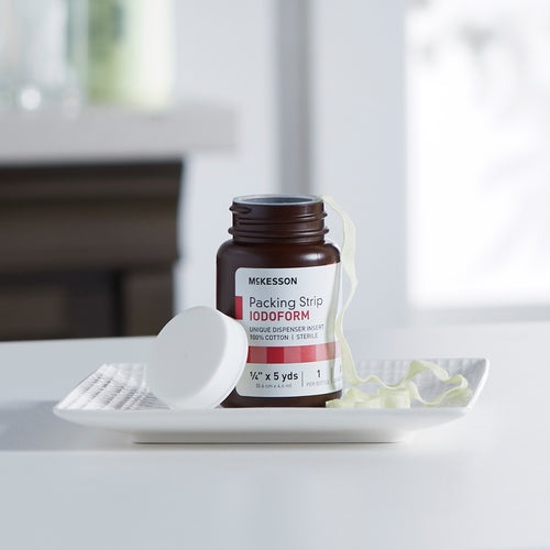McKesson iodoform wound packing strip in open amber bottle with gauze strip pulled out, lid beside it on white tray