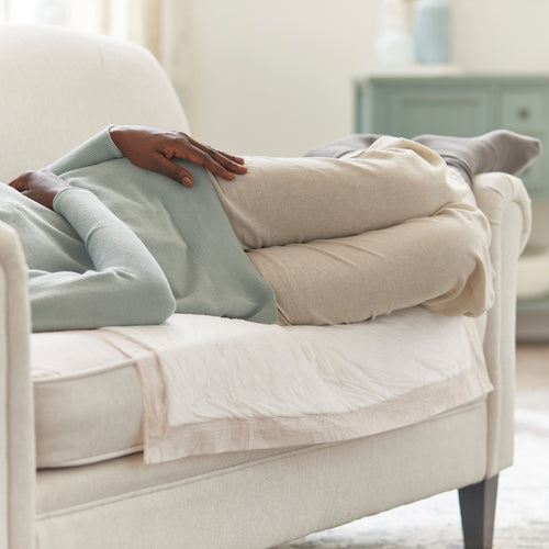 Disposable underpad laid flat on a white sofa cushion beneath a person lying on their side