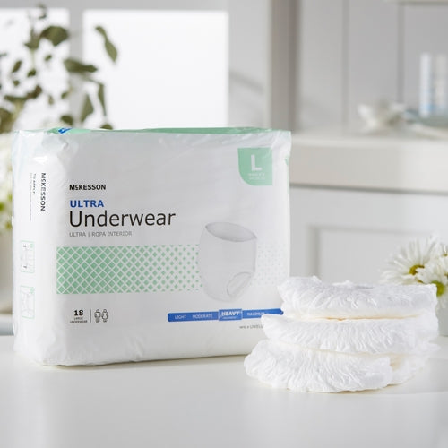 McKesson Ultra absorbent underwear package in large size next to a stack of three folded pull-up briefs on a white surface