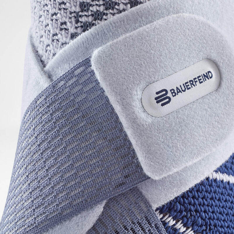 Ankle brace close-up showing Bauerfeind logo on a soft velcro strap over blue and gray knit fabric support
