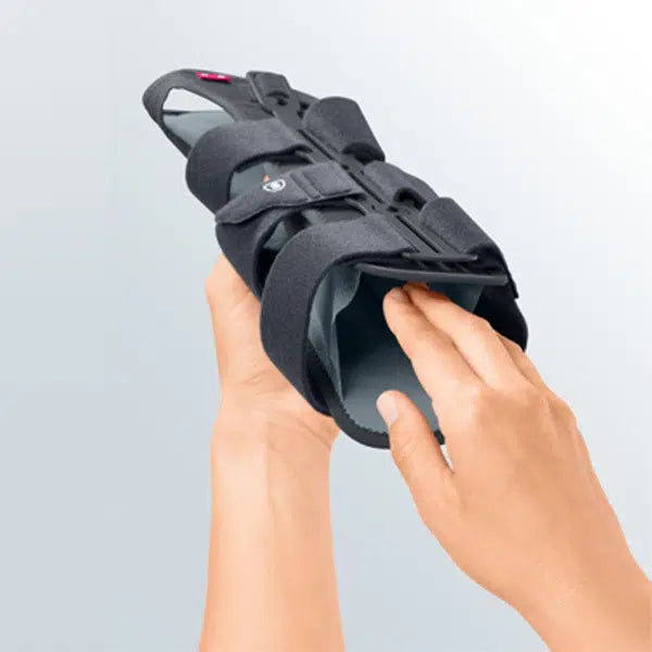 Wrist fracture brace with rigid frame and hook-and-loop straps held in two hands against a light gray background