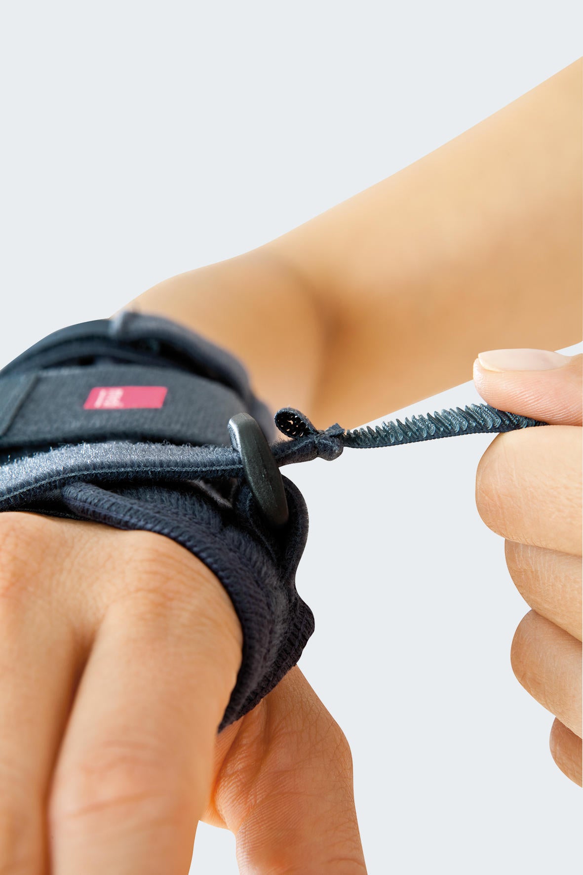 Premium wrist brace being fastened on a wrist, with fingers pulling a serrated adjustable strap through a metal ring closure