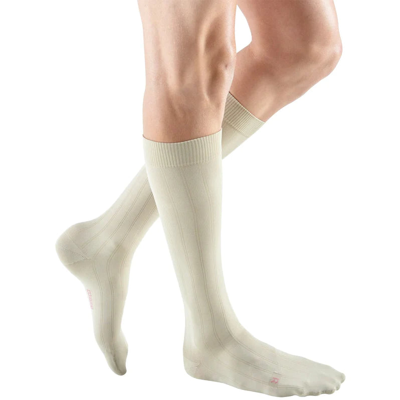 Knee-high compression socks in cream with ribbed texture and banded cuff, shown worn on both legs against white background