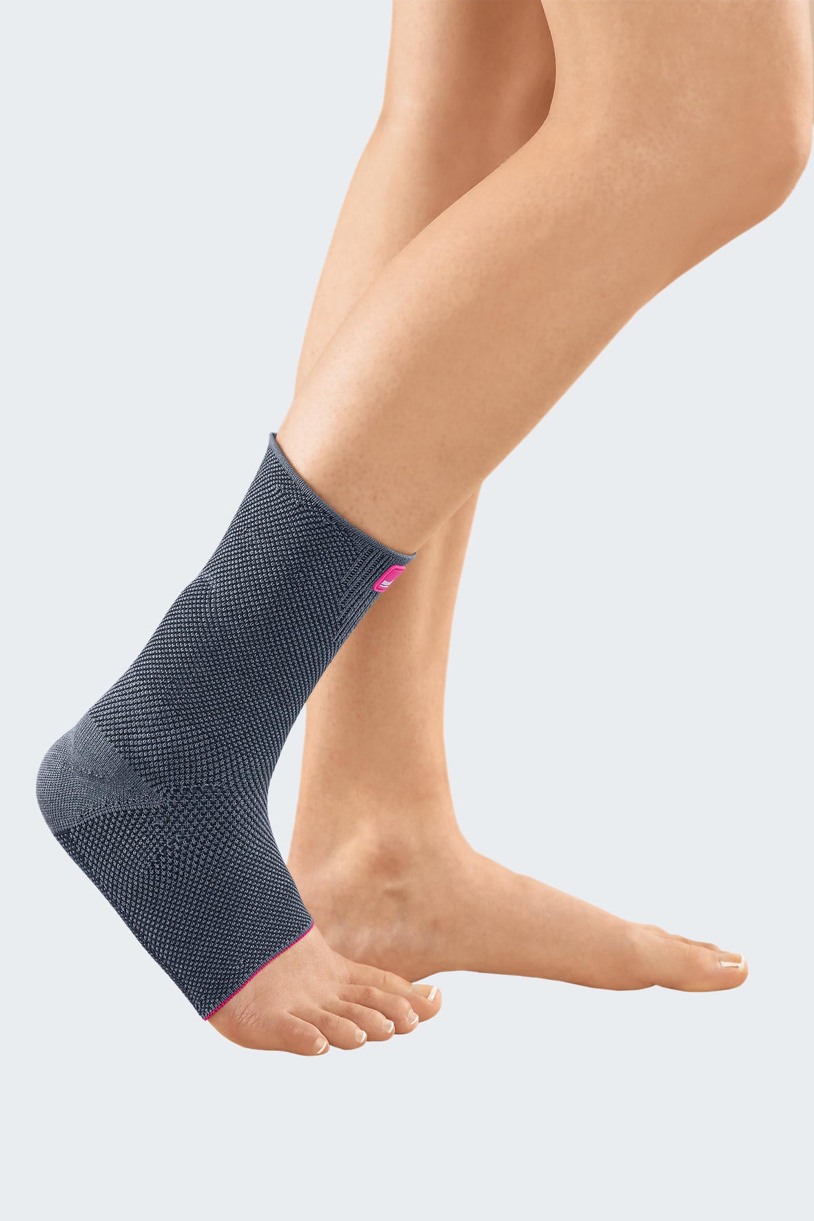 Ankle support in gray knit fabric with pink trim worn on a bare foot, shown from the side on a light background