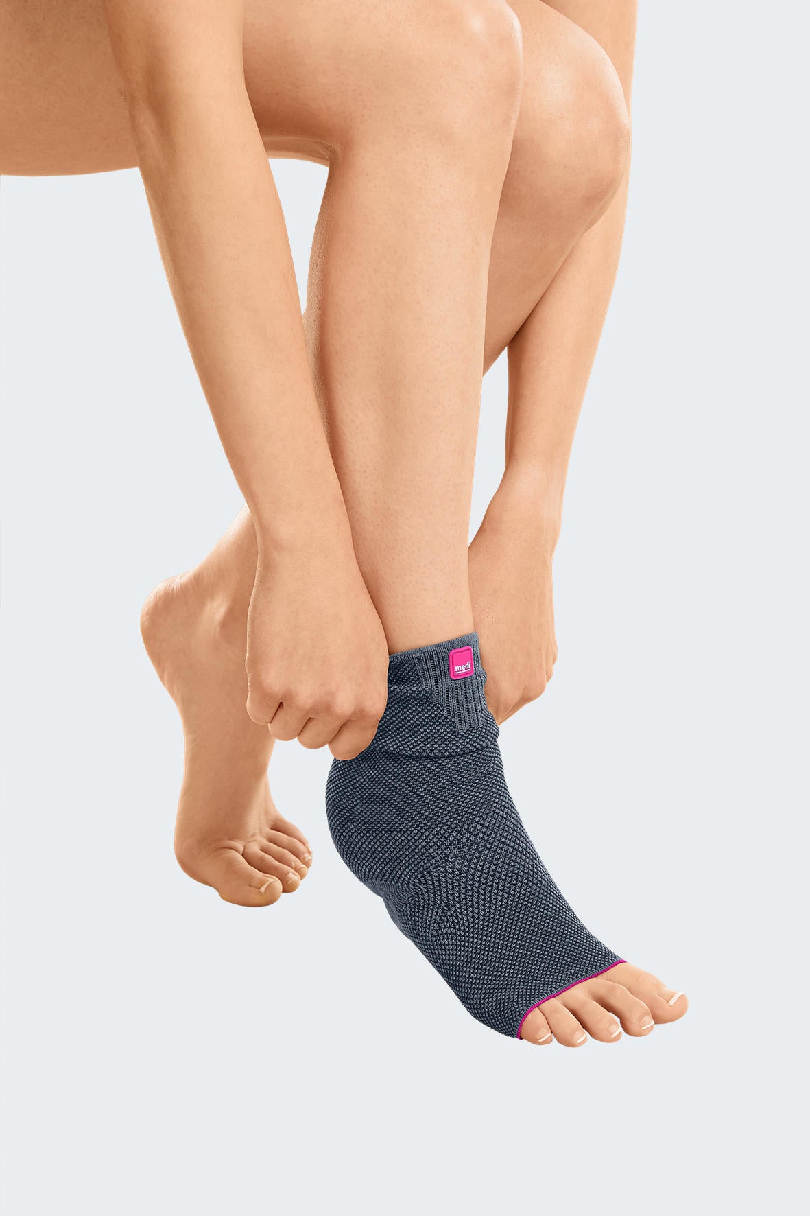 Achimed ankle support in gray knit fabric with pink trim, shown being pulled onto a bare foot and ankle