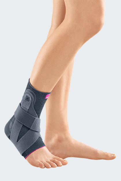 Ankle brace in gray knit fabric with pink accents and adjustable straps, worn on a bare foot and lower leg