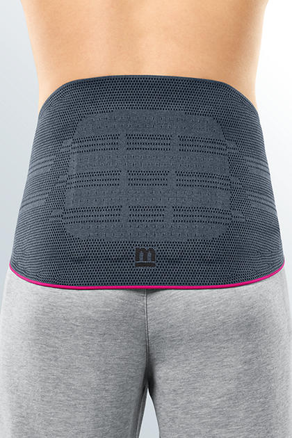 Lumbar support brace in gray breathable mesh with pink trim, worn on a person's lower back over gray pants