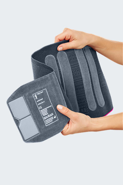 Lumbar support brace held open by two hands showing interior stays and mesh fabric construction, gray with pink trim