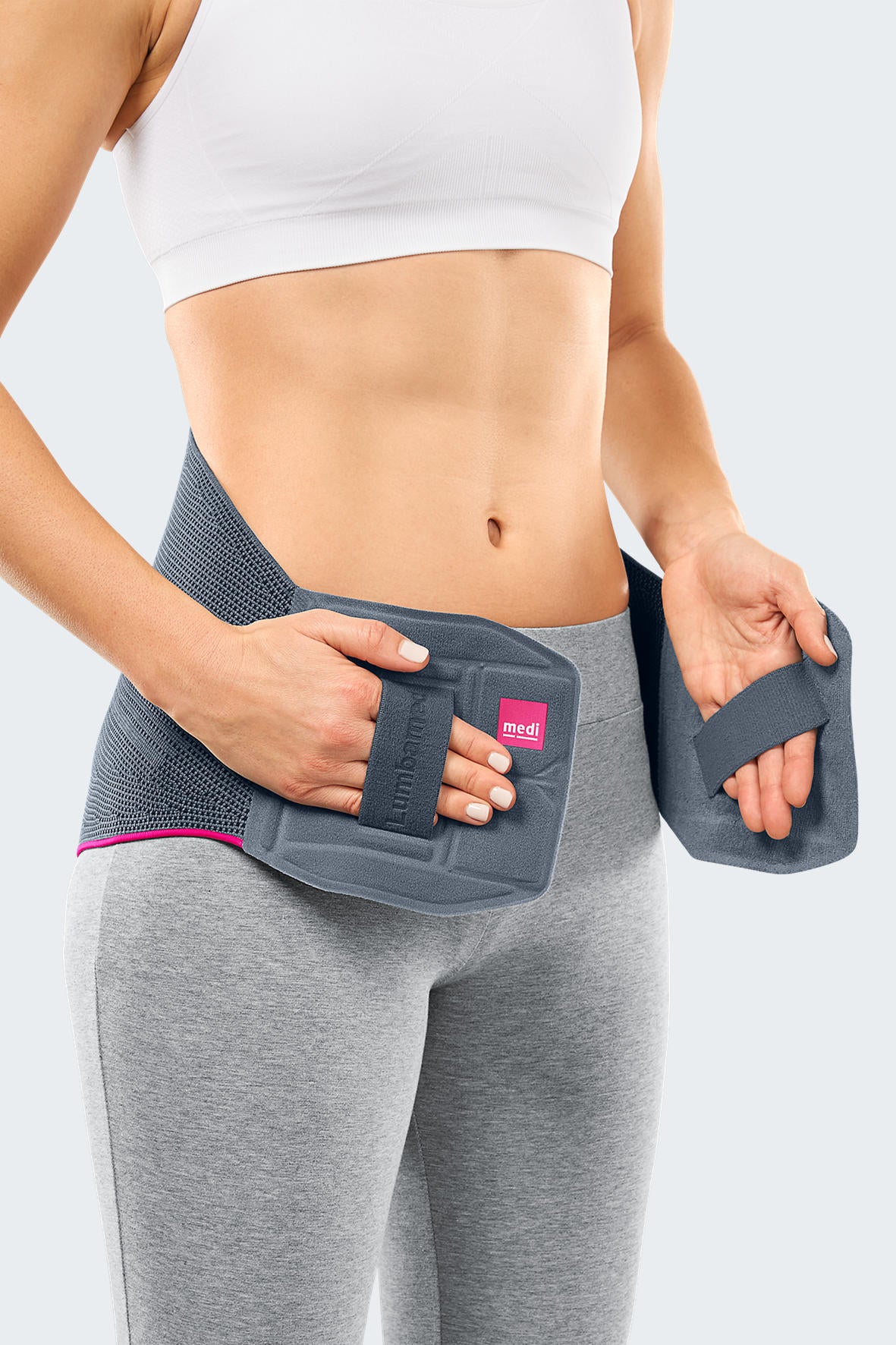 Lumbamed Basic lumbar support belt in gray with pink trim, shown being fastened around a woman's lower back