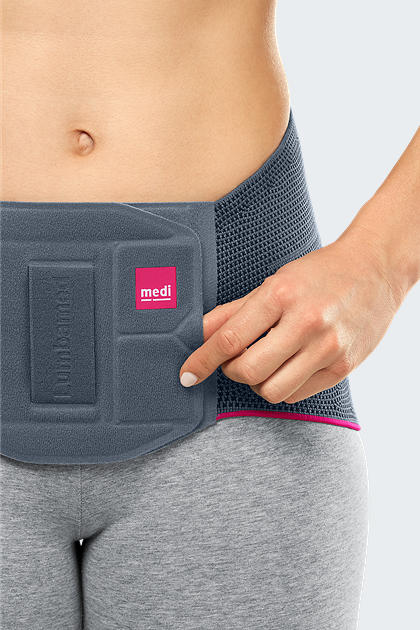 Lumbar support brace in gray with pink trim worn around a woman's waist, shown with hand adjusting the front panel