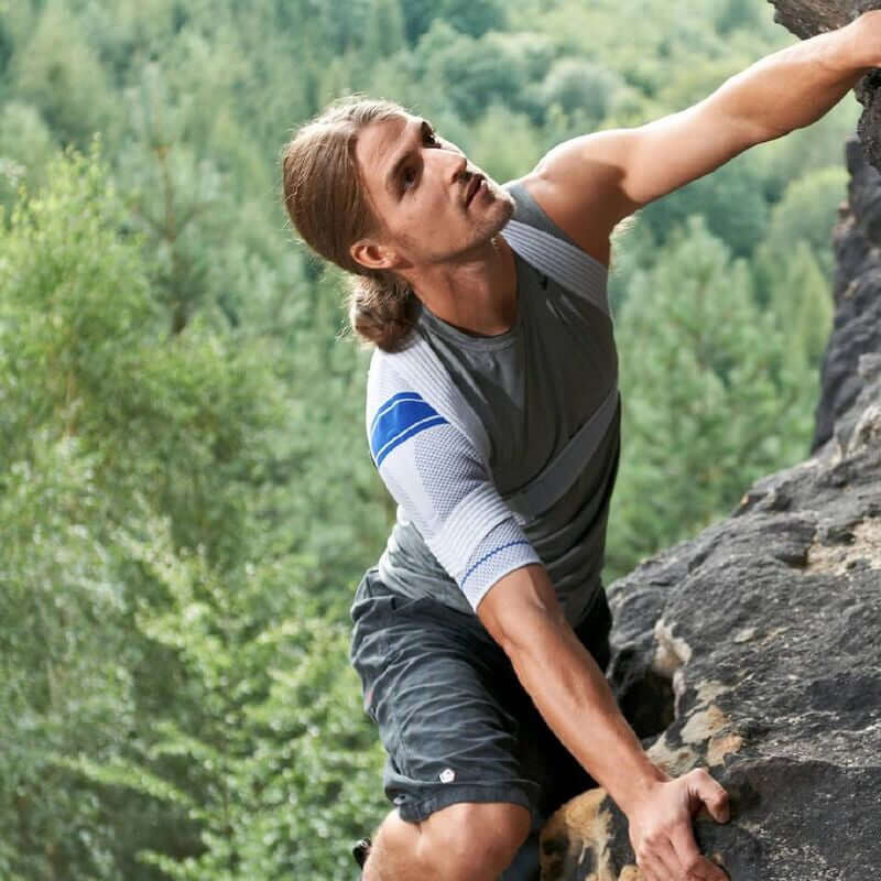 Shoulder brace worn by a man rock climbing outdoors, white and gray knit sleeve with blue stripe detail on left shoulder