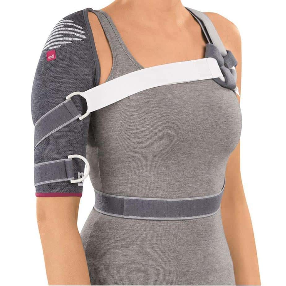 Omomed shoulder support brace in gray with white chest strap and adjustable buckles, worn on left shoulder over gray tank top