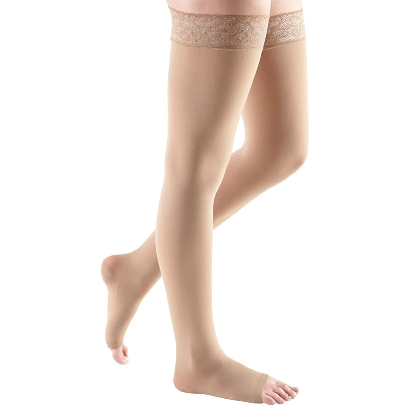Thigh-high compression stockings in beige with lace silicone top band and open toe, shown on a person's legs