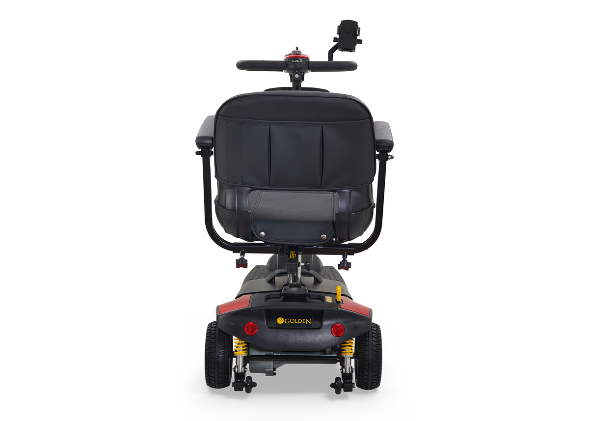 Power mobility scooter rear view showing black padded seat, tiller with device mount, red body panels, and yellow suspension