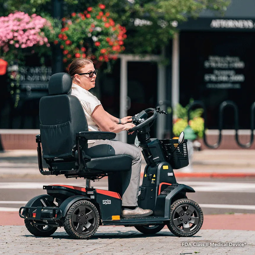 Pride PX4 heavy-duty 4-wheel mobility scooter ridden by a woman outdoors on a brick sidewalk near a downtown street