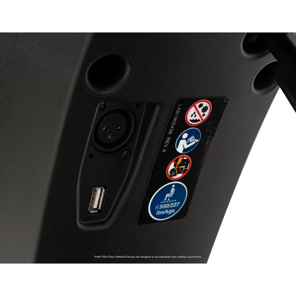 Power wheelchair charging port panel showing XLR connector, USB port, and safety label stickers on black plastic housing