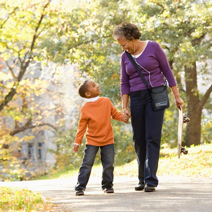 Portable oxygen concentrator worn in shoulder carry bag by woman walking outdoors with a child in an autumn park