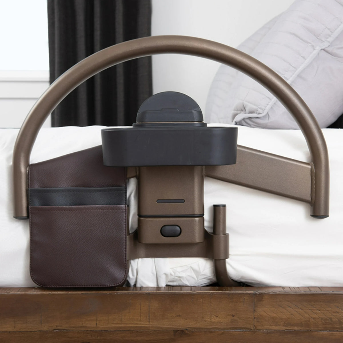 Bed safety rail with arched bronze handle, organizer pouch, and cup holder attachment, mounted on a white bed with wood frame