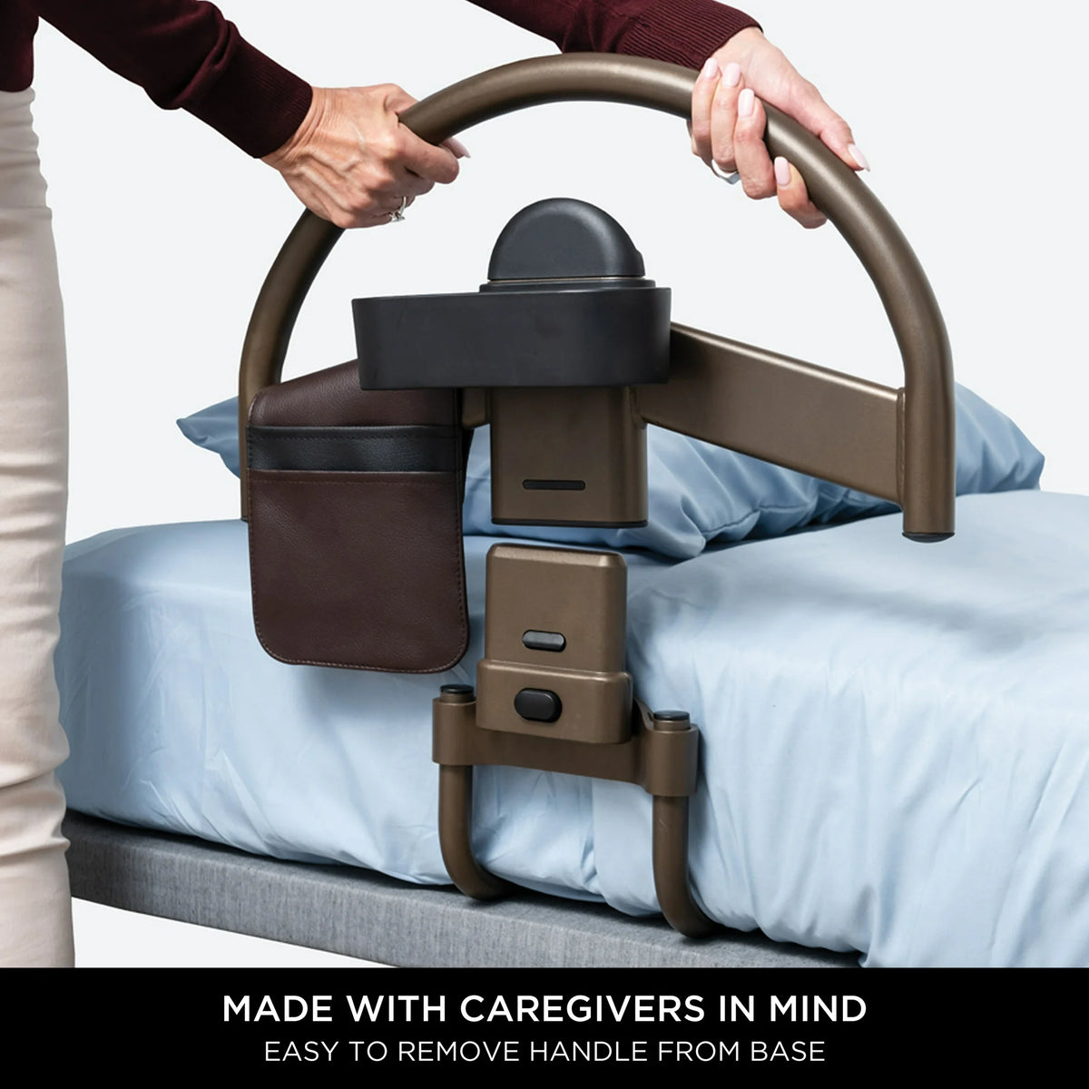 Bed safety rail with arched bronze handle being lifted from base by two hands, with attached side pocket, mounted on bed