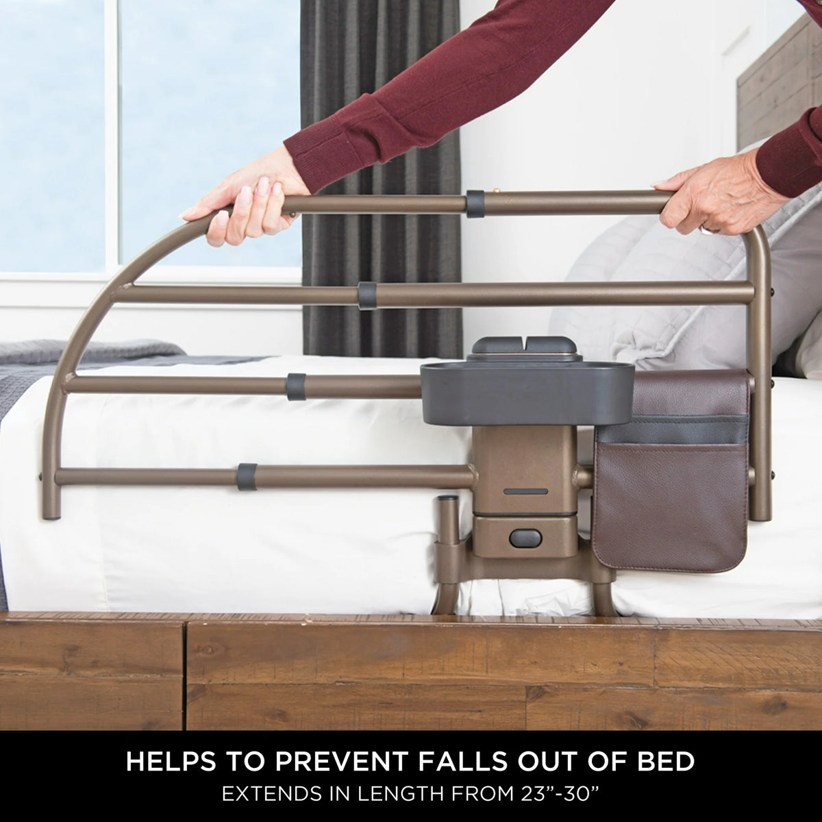 Bed rail with bronze tubular frame, side organizer pouch, and cup holder, shown being gripped by a person on a white mattress