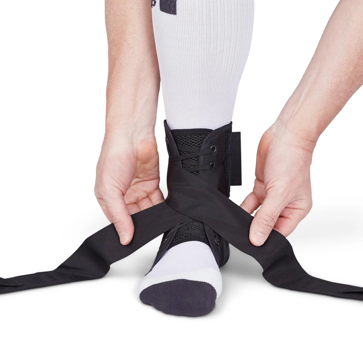 Ankle brace with lace-up closure and figure-8 straps being applied over a white sock and knee-high sock