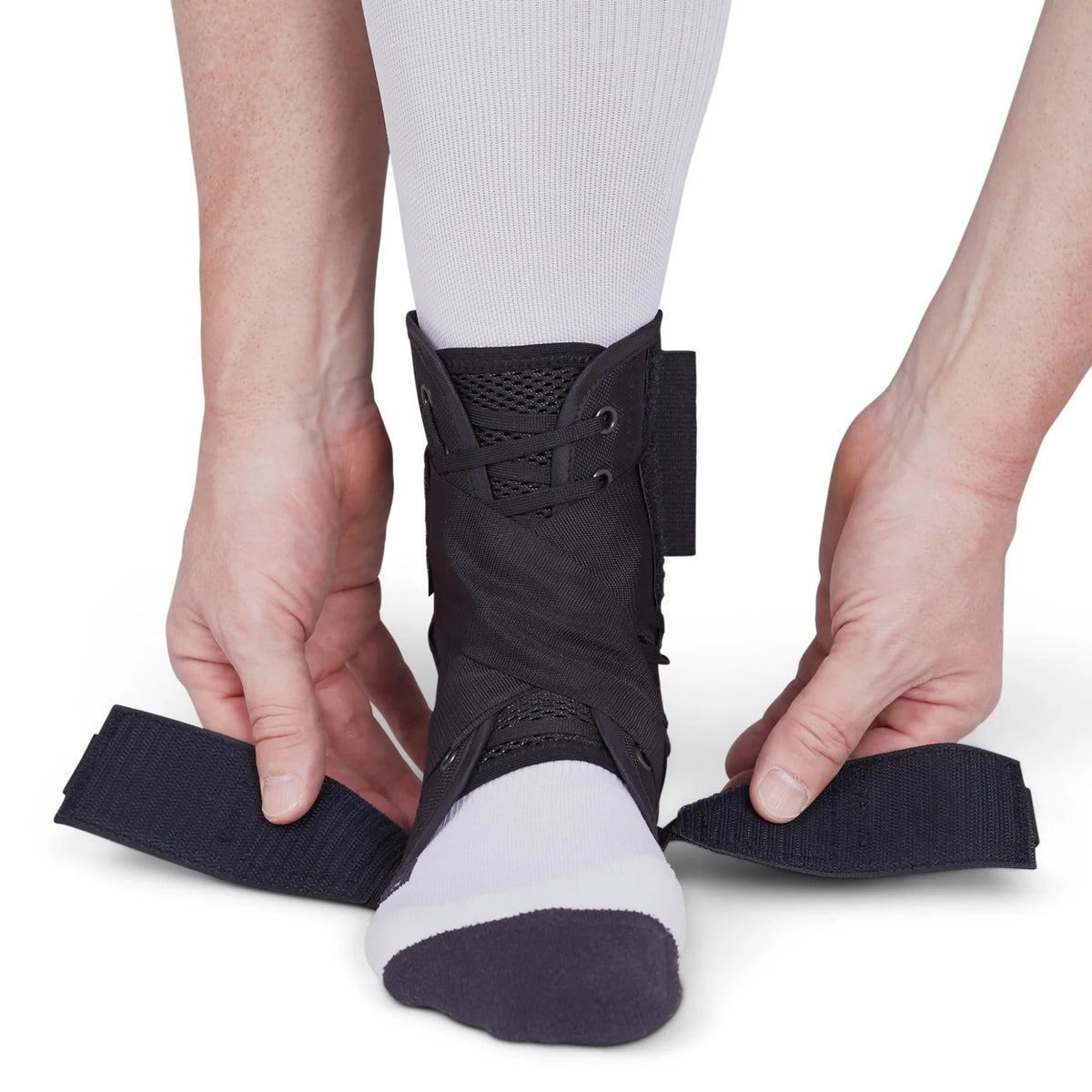 Ankle brace with lace-up closure and hook-and-loop straps being secured around a socked foot and lower leg
