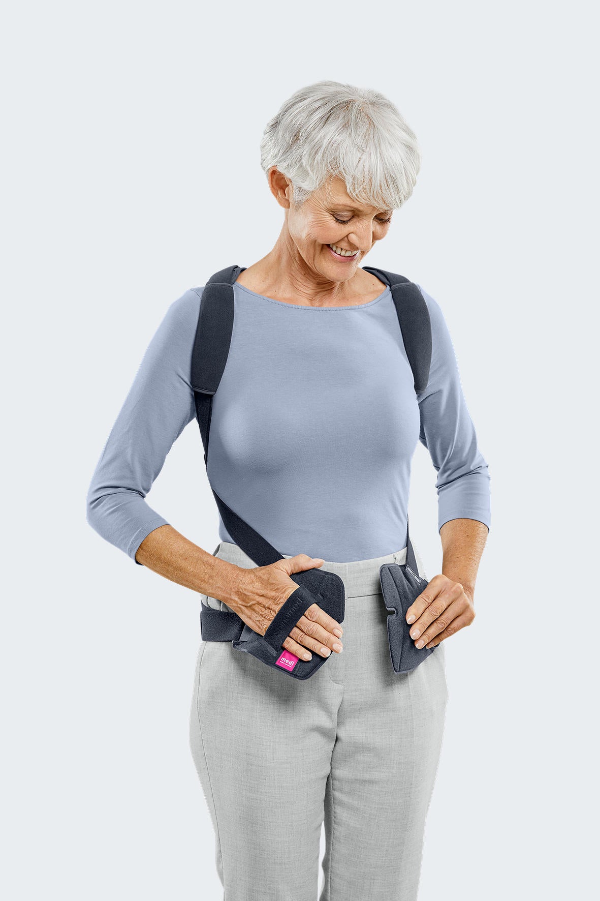 Spinomed spine brace worn by older woman, showing dark gray shoulder straps and waist belt being fastened at the front