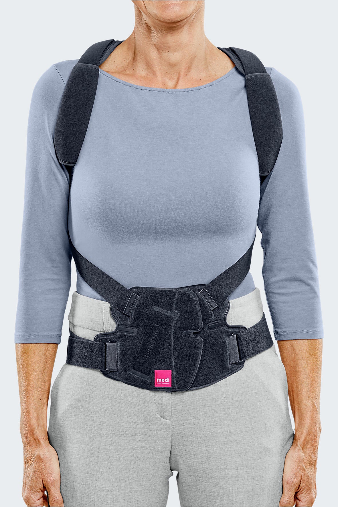 Spinomed spine brace worn by a woman, showing black lumbar belt with shoulder straps and front closure panel