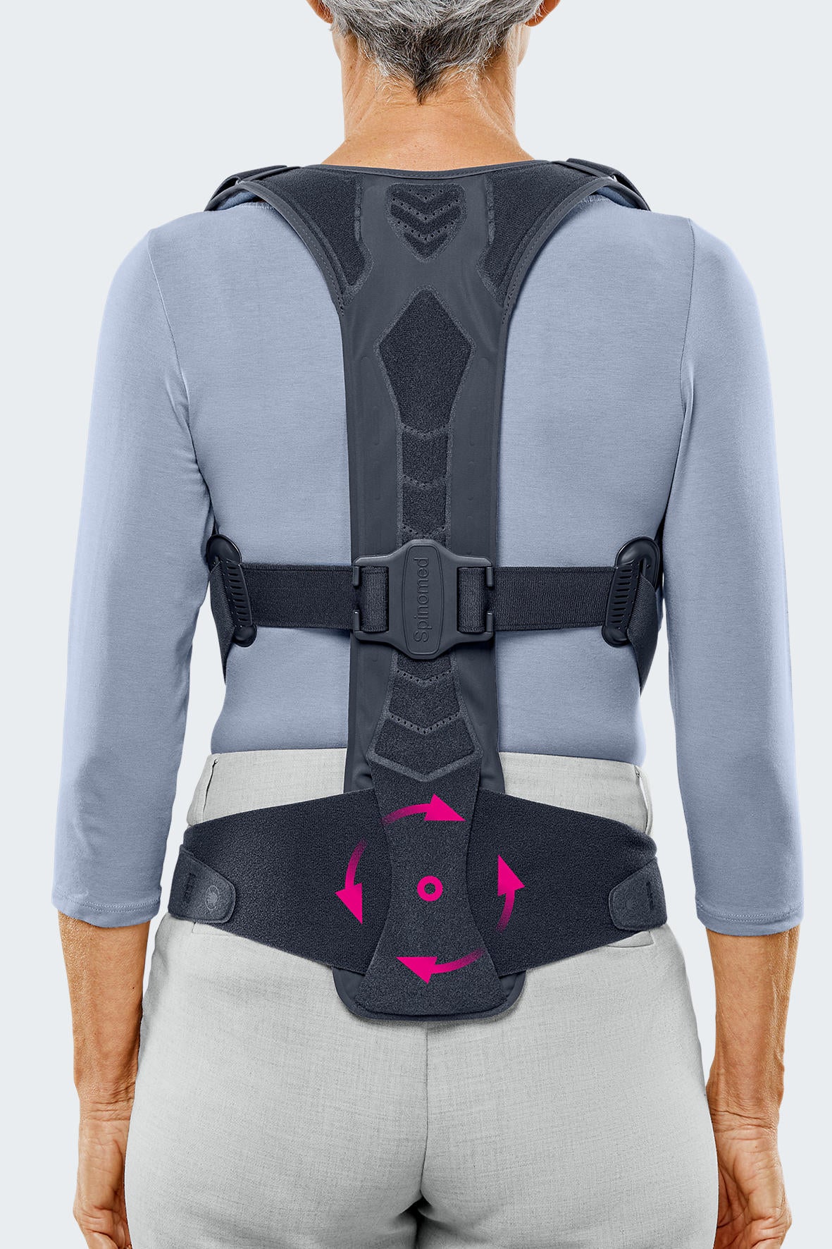 Spinomed spine brace worn by a woman, rear view, showing dark gray back panel, shoulder straps, waist belt with center