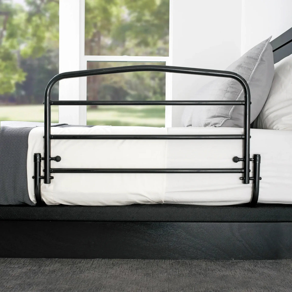 Bed rail with black steel tubular frame and arched top, secured to the side of a white mattress on a dark bed frame