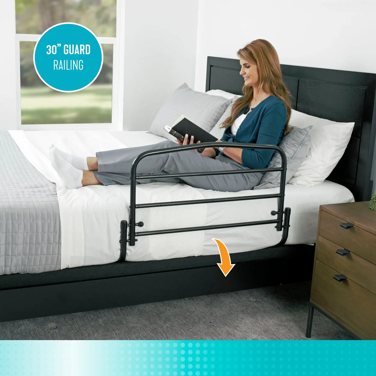 Bed rail guard railing in black metal mounted on a white bed, with a woman reading nearby in a bedroom setting