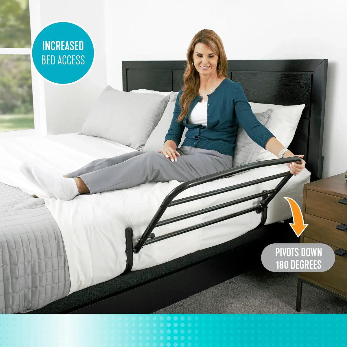 Stander 30" Safety Bed Rail in black steel mounted on a bed, shown in lowered position as woman sits on edge gripping the