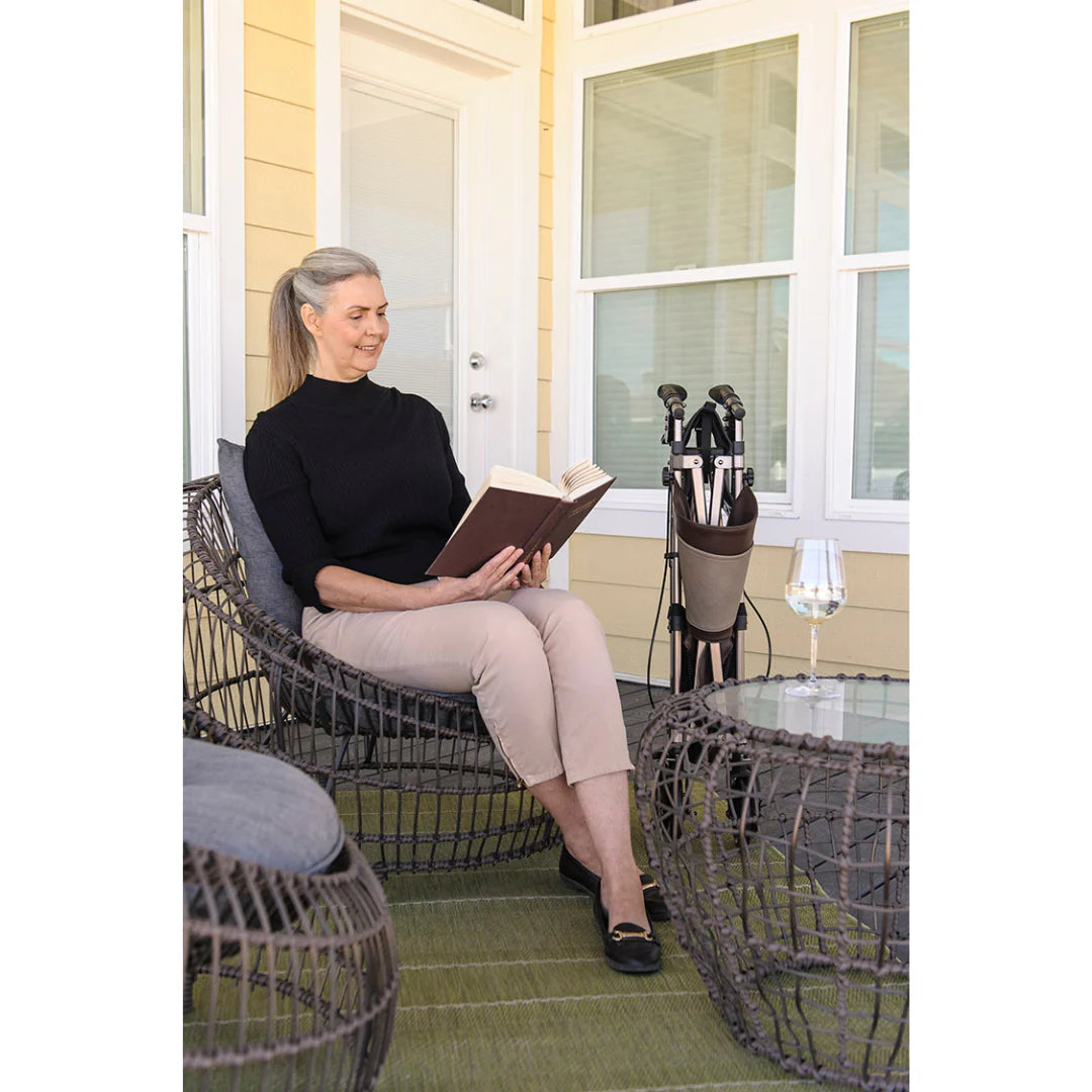 Rollator folded and stored upright beside a woman reading on a patio, shown in lifestyle setting