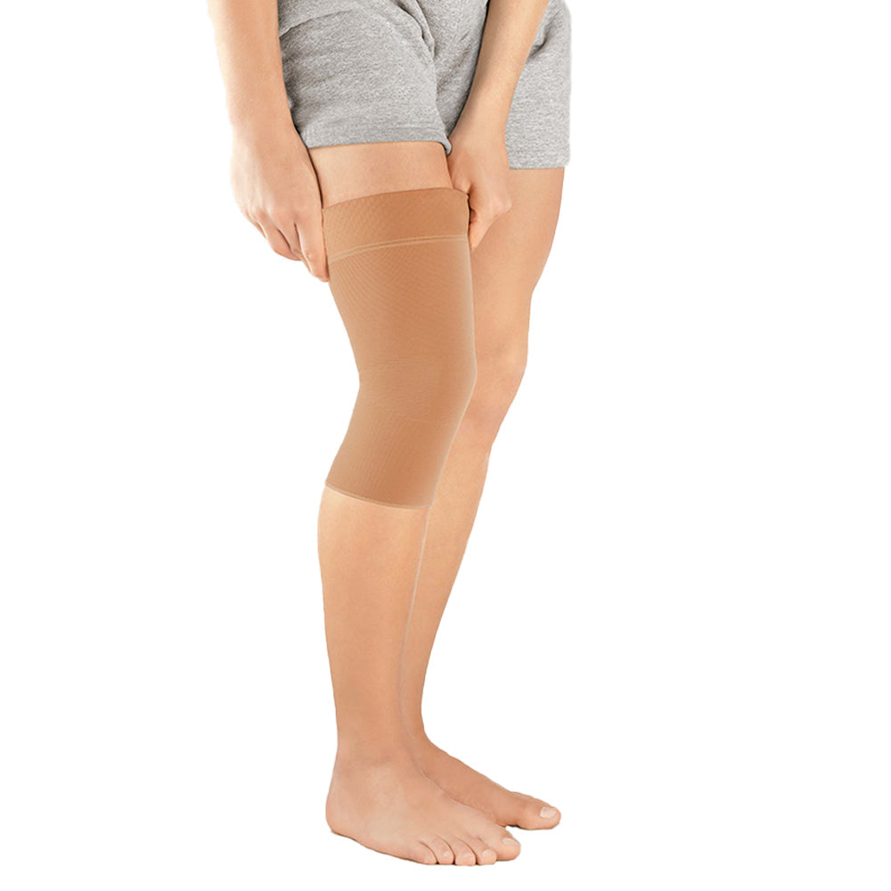 Knee support sleeve in beige worn on a person's leg, shown from thigh to mid-calf, side view
