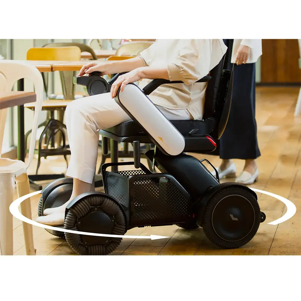 Power wheelchair with user seated indoors, showing 360-degree turning radius graphic around the four black wheels