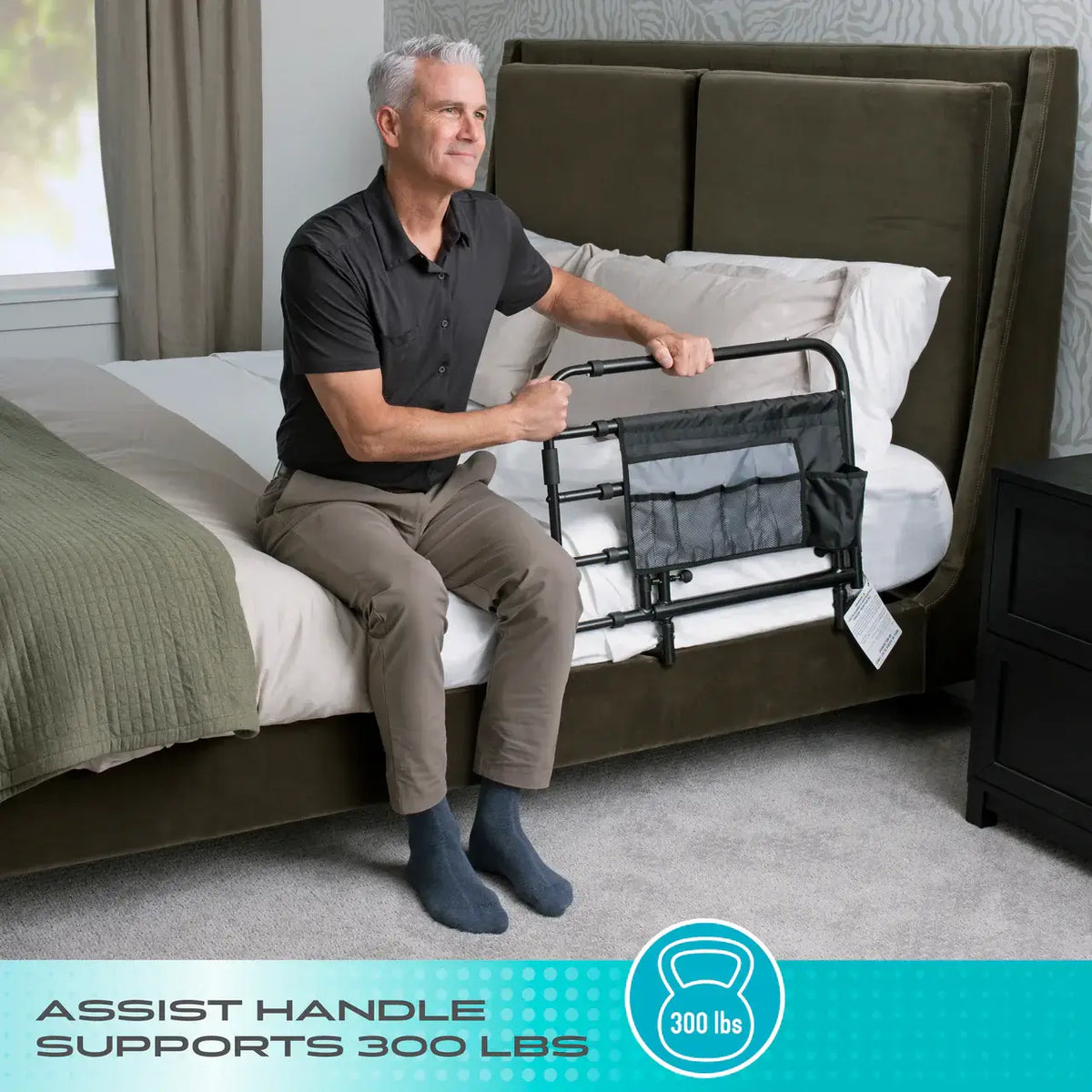Bed rail with black metal frame and mesh storage pouch attached to bedside, used by man sitting on edge of bed