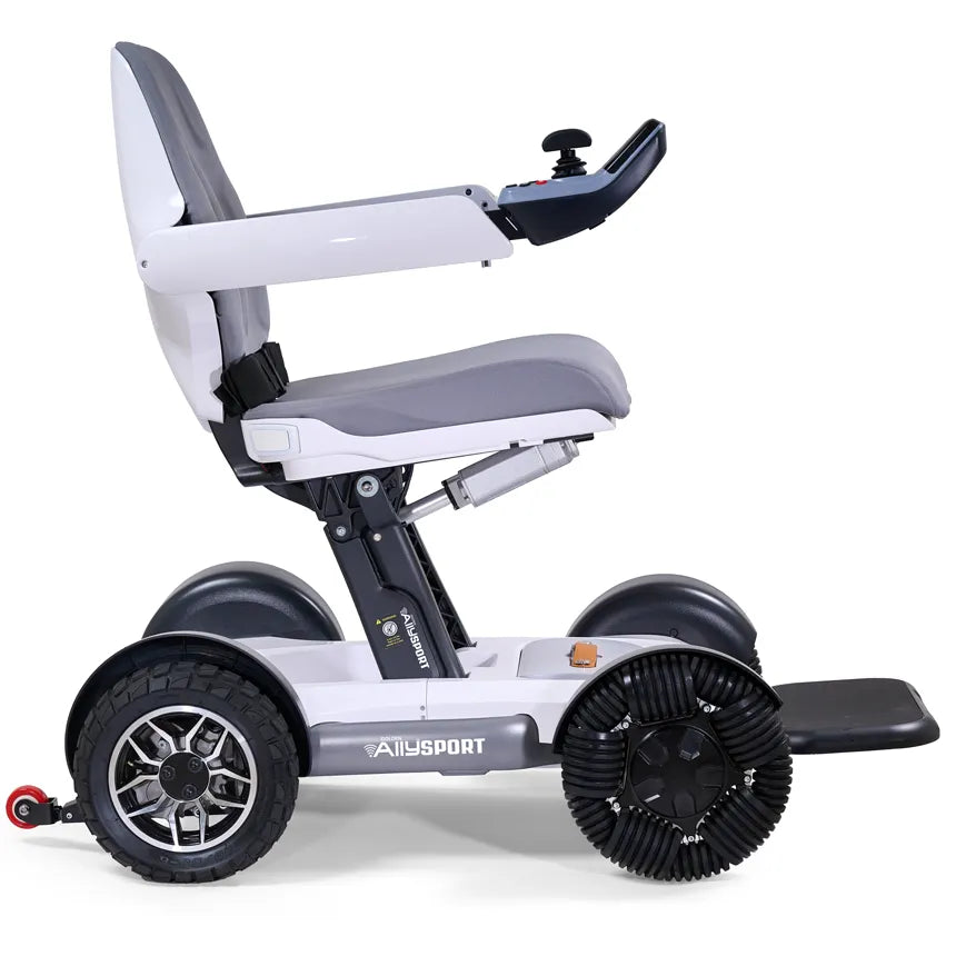Power wheelchair with white frame, gray padded seat, joystick controller, footrest, and four large all-terrain wheels, shown