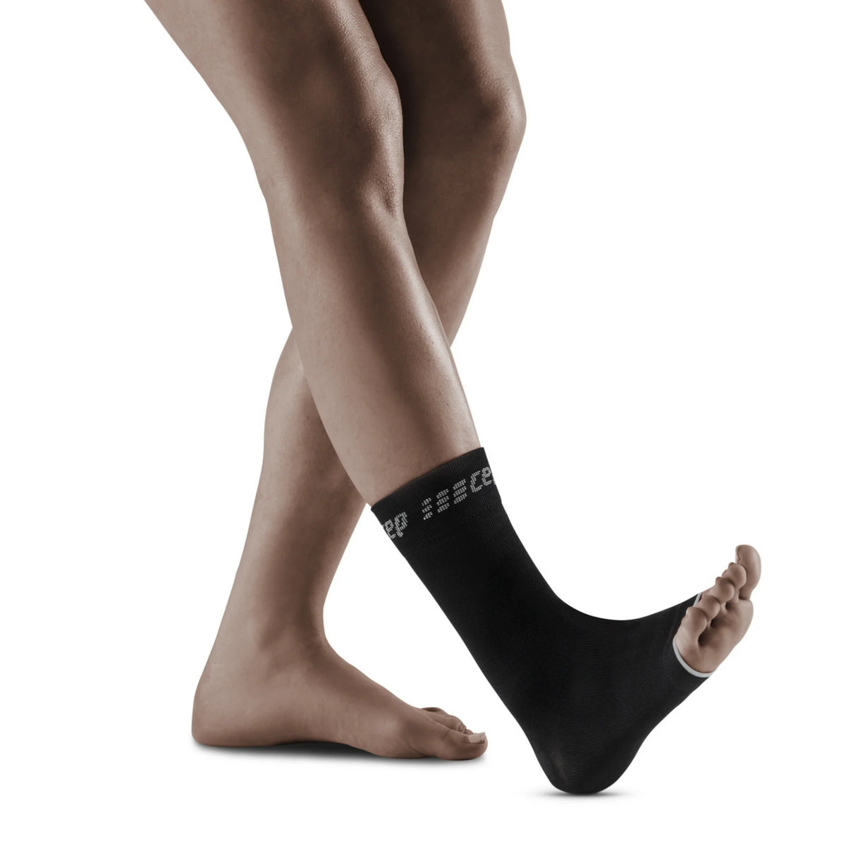 Compression ankle sleeve in black with gray logo text, shown on a person's ankle, open-toe design