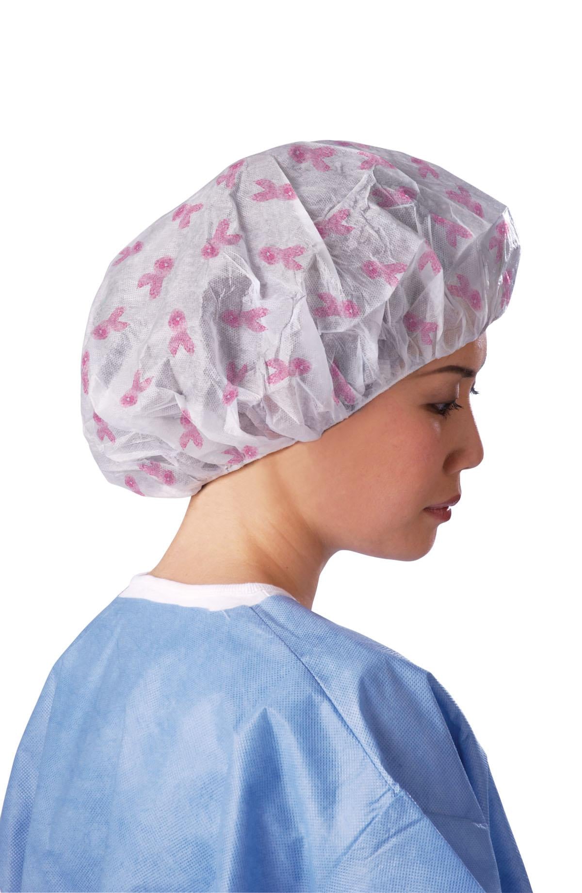 Disposable bouffant cap with pink ribbon print worn by a woman in a blue medical gown, side profile view