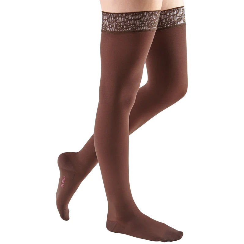 Thigh-high compression stockings in brown with decorative lace silicone top band, shown on a woman's legs against white