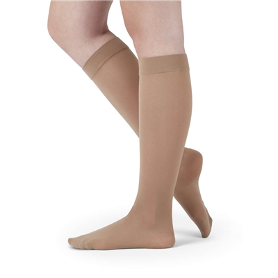 Knee-high compression stockings in beige with a wide silicone top band, shown on a person's lower legs, closed toe style