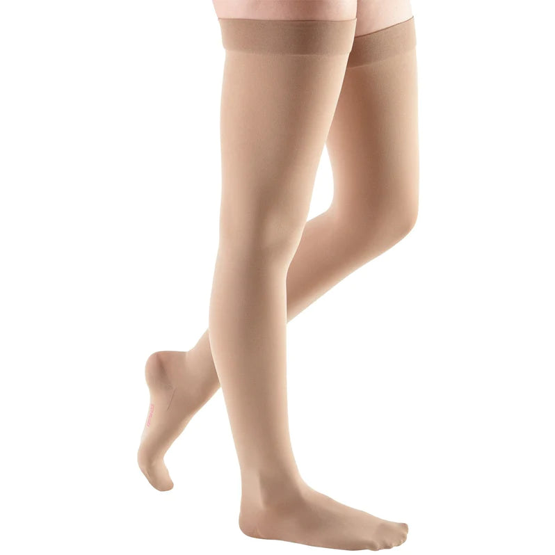 Compression thigh-high stockings in beige worn on a woman's legs, shown from the waist down against a white background