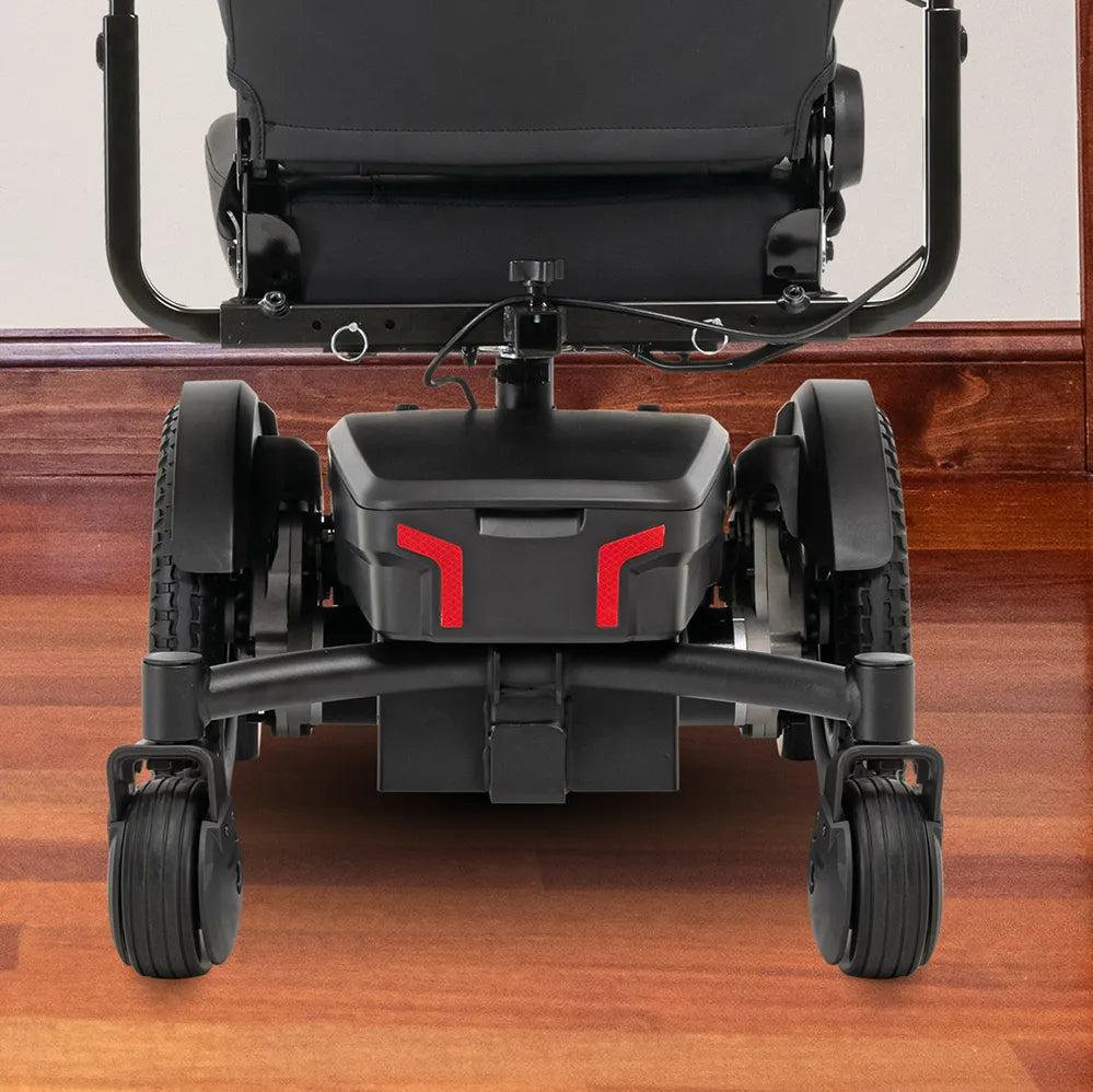 Power wheelchair rear view showing black frame, battery housing with red reflectors, rear drive wheels, and front caster