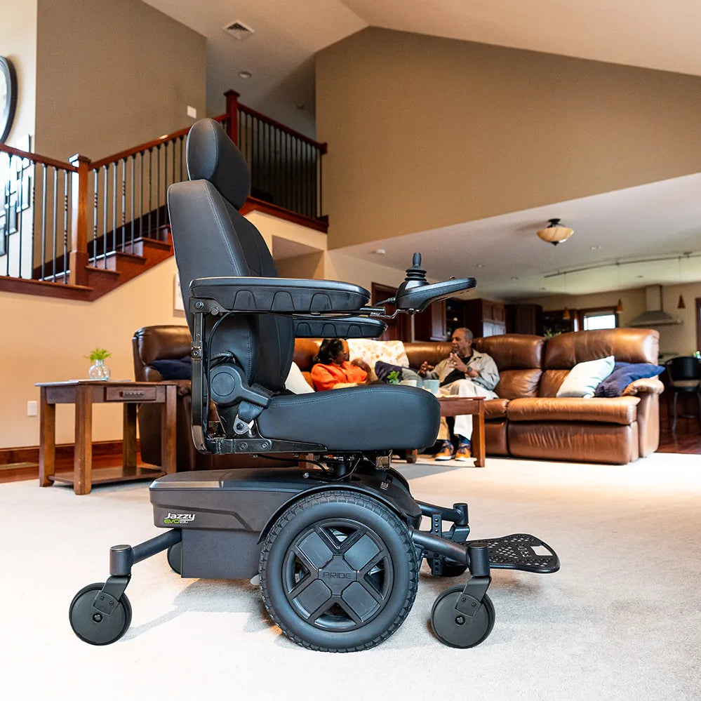 Power wheelchair with black captain's seat and joystick controller displayed in a home living room with two people seated on