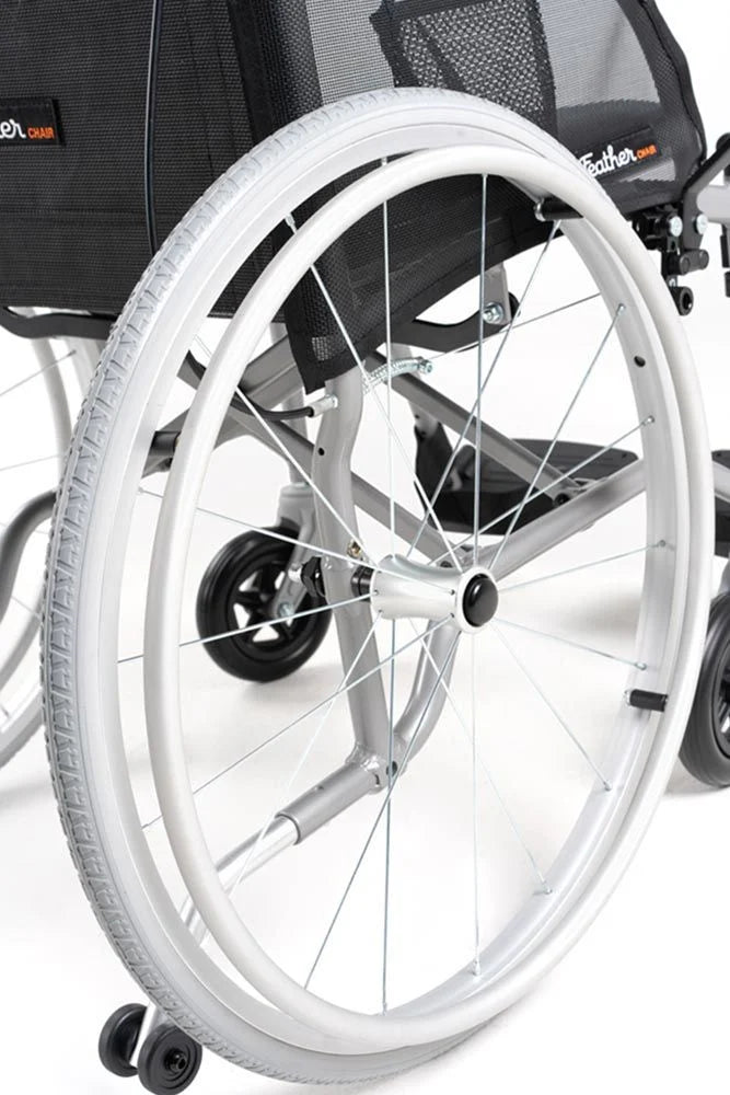 Lightweight wheelchair close-up showing white spoked rear wheel, silver frame, black mesh upholstery, and small front caster
